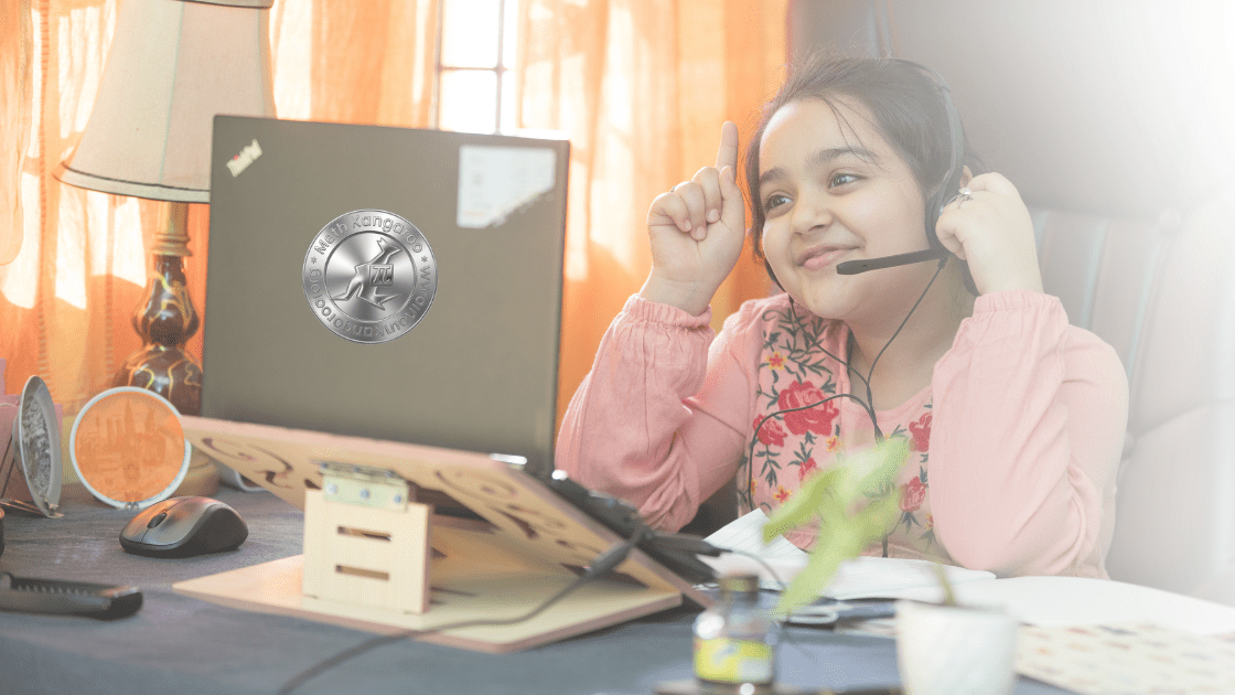 Smiling girl with a headset sits at a desk with a laptop during an online learning session at home, raising her index fingers in a playful gesture.